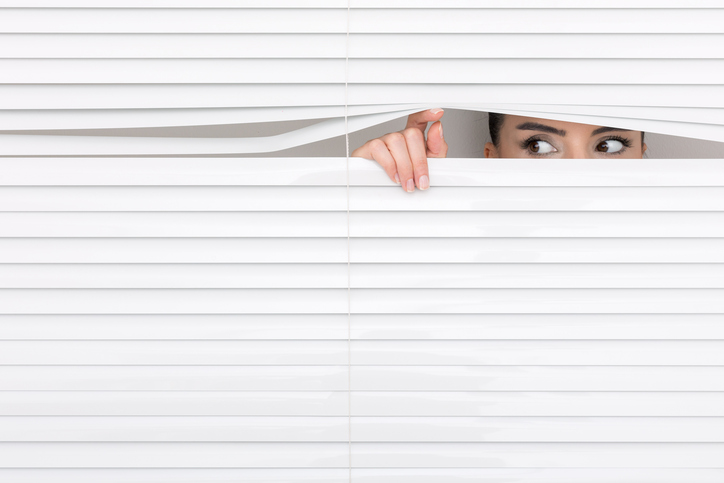 woman looking through window blinds